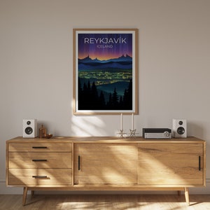 May include: A framed poster featuring a cityscape illustration of Reykjavik, Iceland. The poster has a dark blue background with a purple and orange gradient. The city is depicted in silhouette with lights illuminating the buildings. The text "REYKJAVIK" and "ICELAND" is printed in white at the top of the poster.