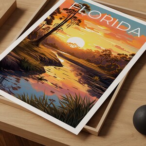 K&ouml;nnte beinhalten: Ein Vintage-Reiseposter mit einem Sonnenuntergang &uuml;ber einem Fluss in einem Sumpf in Florida. Das Poster tr&auml;gt das Wort "FLORIDA" in gro&szlig;en wei&szlig;en Buchstaben oben.