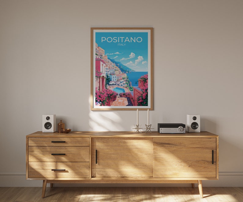 Może przedstawiać: Ramka z plakatem przedstawiającym kolorową ilustrację Positano we Włoszech. Plakat wisi na białej ścianie nad drewnianym regałem z dwoma głośnikami i systemem stereo.