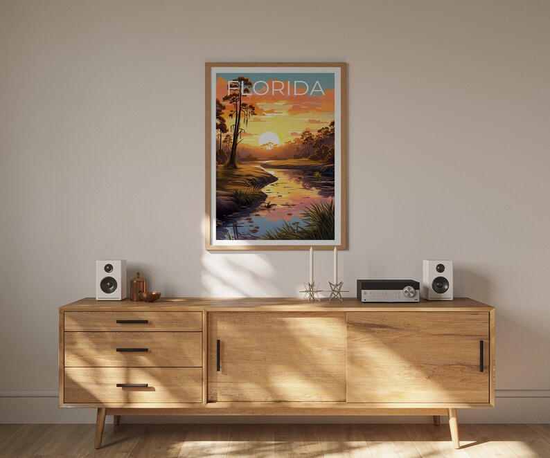K&ouml;nnte beinhalten: Ein Holzschr&auml;nkchen mit drei Schubladen und einer Schiebet&uuml;r. Der Schrank steht in einem Raum mit einem gerahmten Poster, auf dem "FLORIDA" steht und ein Sonnenuntergang &uuml;ber einem Fluss abgebildet ist. Auf dem Schrank stehen zwei Lautsprecher und ein kleines silbernes Objekt in der Mitte.