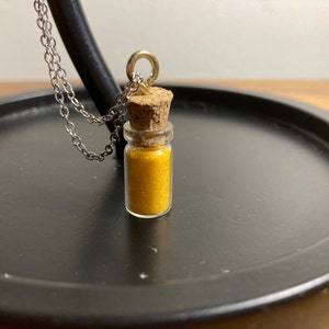 May include: A gold necklace with a small glass bottle filled with yellow glitter. The bottle has a cork stopper.
