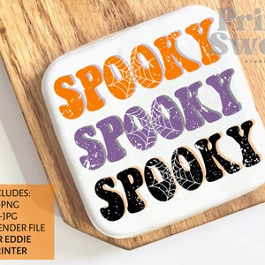 Könnte beinhalten: Weißer Keramikuntersetzer mit den Worten "Spooky Spooky Spooky" in Orange, Lila und Schwarz mit einem Used-Look und Spinnweben.