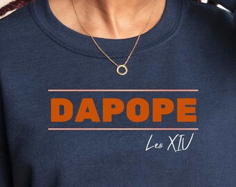 Könnte beinhalten: Marineblaues Sweatshirt mit dem Wort "DAPOPE" in orangefarbenen Blockbuchstaben, unterstrichen mit dünnen orangenen Linien. Darunter steht der Text "Les XIV" in Weiß. Das Sweatshirt hat lange Ärmel und einen Rundhalsausschnitt.
