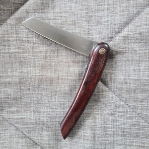 May include: A small, folding pocket knife with a wooden handle. The handle is a dark reddish brown color and the blade is made of stainless steel.