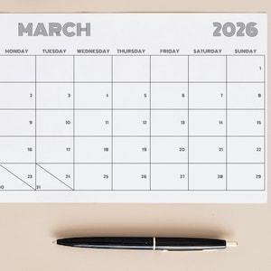 May include: A white calendar for March 2026 with a black pen. The calendar grid is black, with the month and year in a bold, sans-serif font. The days of the week are listed across the top. The pen is black with a silver band.