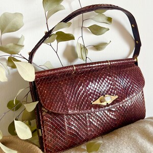 May include: A vintage brown snakeskin handbag with a gold clasp and a bamboo handle.
