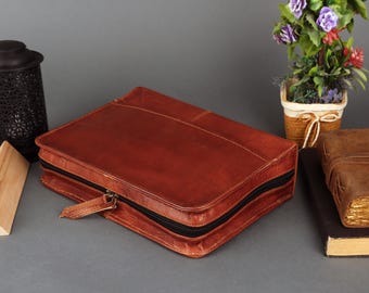 May include: A brown leather zippered case with a black zipper. The case is closed and lying on a gray surface.