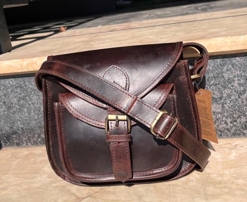 Peut inclure: Un sac &agrave; bandouli&egrave;re en cuir marron avec une fermeture &agrave; rabat et une boucle. Le sac a une poche avant et une longue bandouli&egrave;re r&eacute;glable.