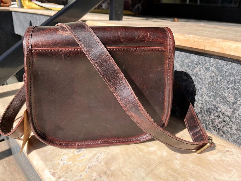 Peut inclure: Un sac &agrave; main en cuir marron avec une longue bandouli&egrave;re r&eacute;glable. Le sac a une fermeture &agrave; rabat et une boucle.