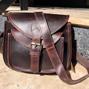 Peut inclure: Un sac &agrave; bandouli&egrave;re en cuir marron avec une fermeture &agrave; rabat et une boucle. Le sac a une poche avant et une longue bandouli&egrave;re r&eacute;glable.
