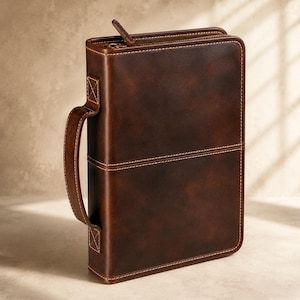 May include: A dark brown rectangular case with a smooth finish and visible stitching along the edges. It features a sturdy side handle attached with reinforced square stitching and a metal zipper closure running along the top edge.