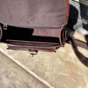 Peut inclure: Un sac &agrave; main en cuir marron avec une fermeture &agrave; rabat et une longue bandouli&egrave;re r&eacute;glable. Le sac est ouvert et l'int&eacute;rieur est doubl&eacute; d'un tissu marron.