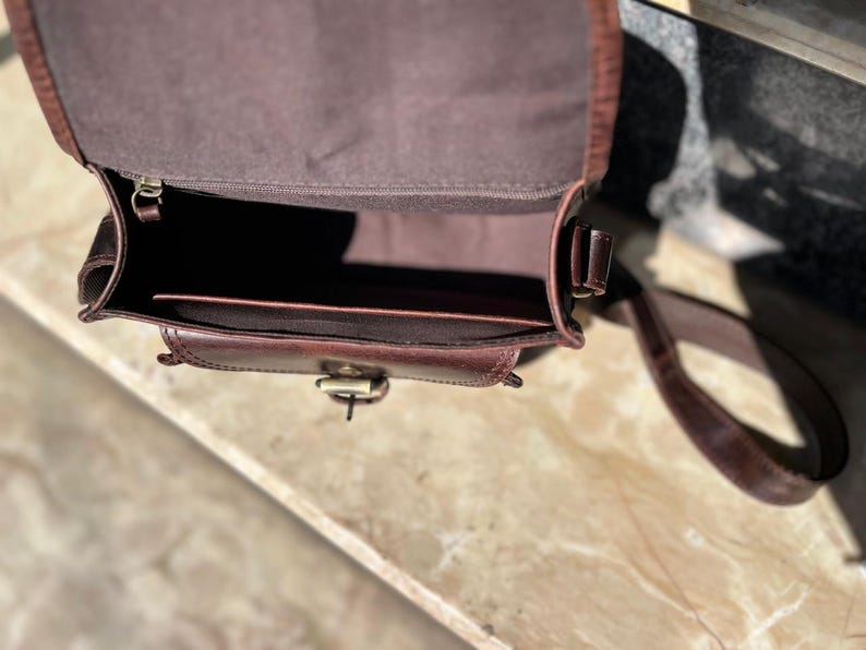 Peut inclure: Un sac &agrave; main en cuir marron avec une fermeture &agrave; rabat et une longue bandouli&egrave;re r&eacute;glable. Le sac est ouvert et l'int&eacute;rieur est doubl&eacute; d'un tissu marron.
