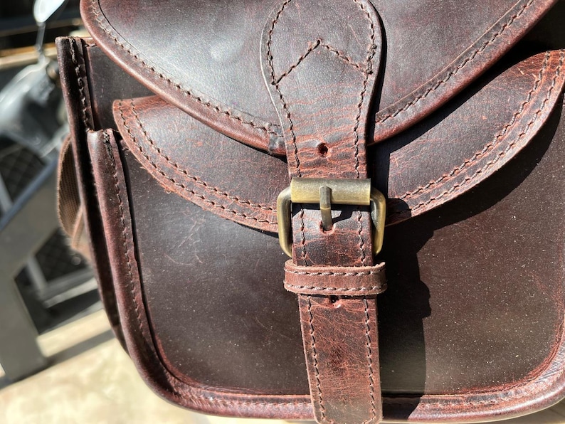 Peut inclure: Un sac &agrave; main en cuir marron avec une boucle en laiton et des d&eacute;tails de couture. Le sac a une fermeture &agrave; rabat et une seule sangle.
