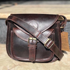 Peut inclure: Un sac &agrave; bandouli&egrave;re en cuir marron avec une fermeture &agrave; rabat et une boucle. Le sac a une poche avant et une longue bandouli&egrave;re r&eacute;glable.