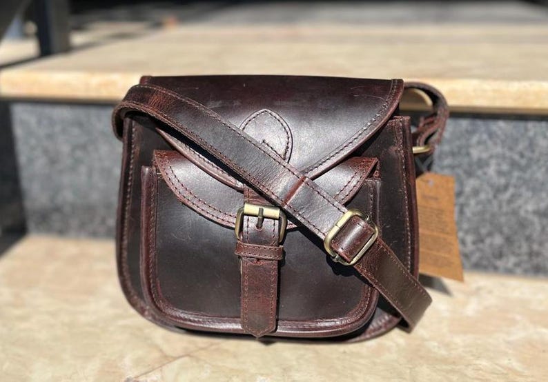 Peut inclure: Un sac &agrave; bandouli&egrave;re en cuir marron avec une fermeture &agrave; rabat et une boucle. Le sac a une poche avant et une longue bandouli&egrave;re r&eacute;glable.