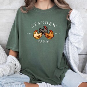 May include: A green t-shirt with a white graphic of three pixelated chickens and the text "Stardew Farm Est. 2016".