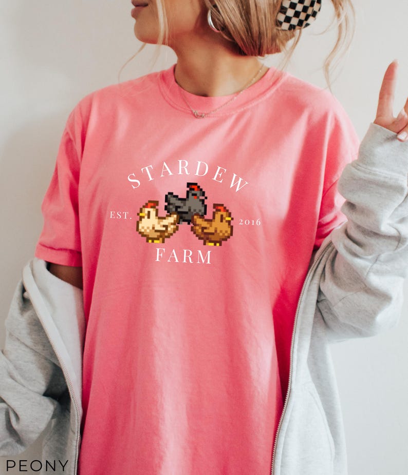 May include: A pink t-shirt with a white graphic of three pixelated chickens and the text "Stardew Farm Est. 2016".