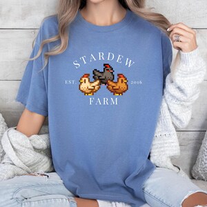May include: A blue t-shirt with a white graphic of three pixelated chickens and the text "Stardew Farm Est. 2016".