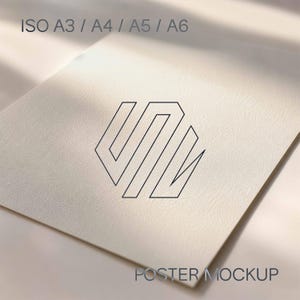 Peut inclure: Une maquette d'affiche en papier blanc textur&eacute; pr&eacute;sentant un logo noir en lignes g&eacute;om&eacute;triques au centre. Le texte ISO A3 / A4 / A5 / A6 est imprim&eacute; en haut, et le texte POSTER MOCKUP est imprim&eacute; en bas dans une police sans empattement gris fonc&eacute;.