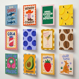 May include: A collection of twelve greeting cards with various designs. The cards feature illustrations of sharks, a cowboy, coffee beans, a martini, and more. Text includes "Big Sharks", "Howdy Cowboy", "More Espresso Less Depresso", "Cola", "Lost in Music", "Avocado", "Raspberry", and "Chill Time".