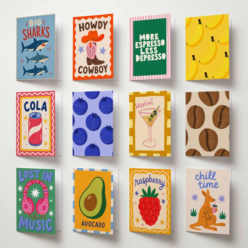 May include: A collection of twelve rectangular greeting cards arranged in a grid. Designs include sharks, a cowboy boot, coffee themes, bananas, a cola can, blueberries, a martini, coffee beans, headphones, an avocado, a raspberry, and a kangaroo.