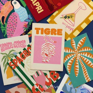 May include: A collection of colorful art prints with travel and food themes. Designs include a tiger, a martini, a toucan, and a palm tree. The prints feature bold colors and graphic illustrations, with text such as "TIGRE" and "Venice Canals".