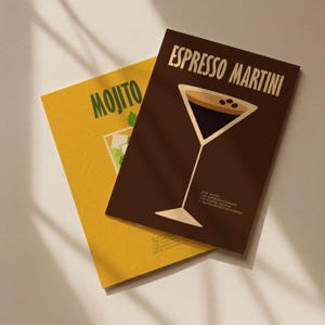 Op de afbeelding: Twee cocktailreceptprints. De "Espresso Martini" print is bruin met een martini glas illustratie en recept. De "Mojito" print is geel met een mojito illustratie en recept. De prints zijn schuin op een wit oppervlak.