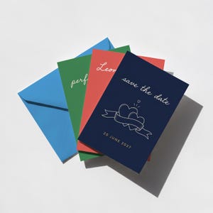 May include: A collection of colorful save-the-date cards and envelopes. The cards are in red, green, and navy blue, with white text and illustrations. The navy card says "save the date" with two hearts and a ribbon. The blue envelope is on the left.