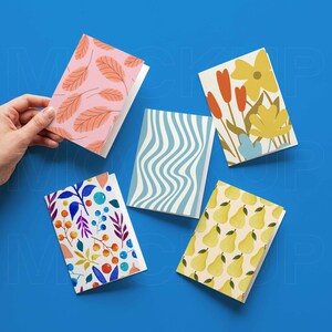 K&ouml;nnte beinhalten: F&uuml;nf Gru&szlig;karten mit verschiedenen Designs. Eine Karte zeigt rosa Bl&auml;tter, eine andere blau-wei&szlig;e Wellenlinien und eine dritte gelbe Birnen. Die anderen beiden Karten haben florale Muster.