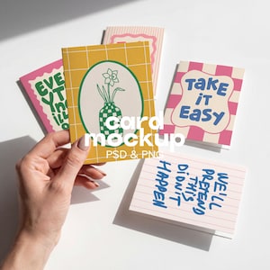 May include: A collection of four rectangular greeting cards featuring various designs. One card displays a yellow grid pattern with a green oval containing a flower in a checkered vase. Other cards feature pink and white patterns with text.