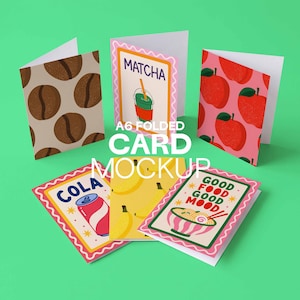 May include: A collection of A6 folded cards with various designs. One card features coffee beans, another has a matcha drink, and a third displays red apples. Other cards show a cola can, bananas, and a bowl of noodles with the text "GOOD FOOD GOOD MOOD".