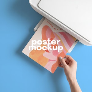 May include: A white printer outputting a rectangular paper sheet featuring an abstract illustration with warm orange, pink, and yellow tones. The text "SUMMER AS A STATE" is printed in red at the top, while the white text "poster mockup" is centered.