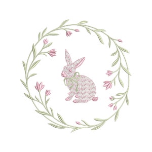 May include: A pink bunny rabbit with a bow sits in the center of a green wreath with pink flowers.