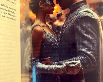 May include: A romantic image of a couple in formal attire, wearing masks. The woman wears a silver dress and a jeweled headpiece. The man is in a silver suit. The number "34" is visible. The background is blurred with warm tones.