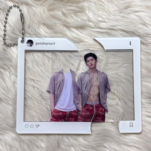May include: A clear acrylic keychain featuring a photo of a person in a light purple shirt and red shorts. The keychain is designed to resemble an Instagram post, with the username "pondnaravit" visible. A silver ball chain is attached.