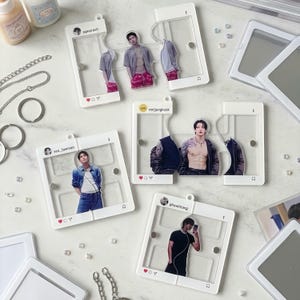 May include: A collection of white acrylic frames designed to resemble social media posts, each featuring a clear centre panel with a printed image of a person. The frames are modular, with magnetic connectors, and include small metal keychains.