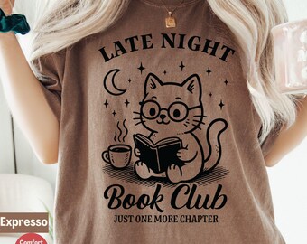 Könnte beinhalten: Braunes T-Shirt mit einer schwarzen Grafik einer Katze mit Brille, die ein Buch liest und Kaffee trinkt. Der Text auf dem Shirt lautet "Late Night Book Club" und "Just One More Chapter".