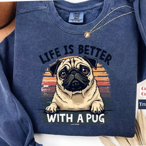 May include: A navy blue sweatshirt with a vintage-style graphic of a pug dog. The text "Life is better with a pug" is printed on the sweatshirt.