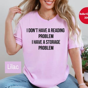 May include: Lilac-colored t-shirt with the text "I DON'T HAVE A READING PROBLEM I HAVE A STORAGE PROBLEM" in black. The shirt is a Bella+Canvas 3001 model.