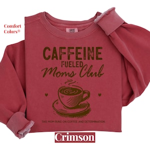 May include: Crimson red sweatshirt with the text "CAFFEINE FUELED MOMS CLUB" and a brown illustration of a coffee cup. The text below the illustration reads "THIS MOM RUNS ON COFFEE AND DETERMINATION".