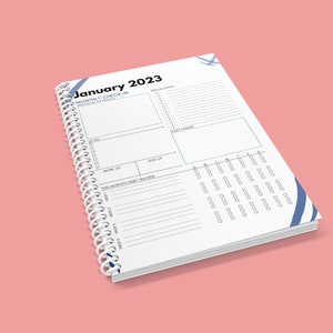 May include: A white spiral bound planner with a blue and white design. The cover says "January 2023" and has a section for a monthly check-in.