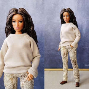 Peut inclure: Une poupée vêtue d'un pull beige et d'un pantalon à imprimé serpent. La poupée a de longs cheveux foncés et est posée devant un fond bleu. La poupée porte des chaussures marron. L'image est bien éclairée et les traits de la poupée sont clairement visibles.