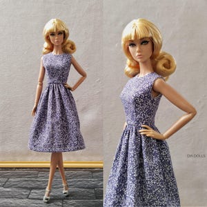 Könnte beinhalten: Eine Puppe in einem ärmellosen, knielangen Kleid mit floralem Muster. Das Kleid ist tiefviolett mit weißen, blattartigen Designs. Die Puppe hat blonde Haare, die in Locken gestylt sind, und trägt silberne Absätze.