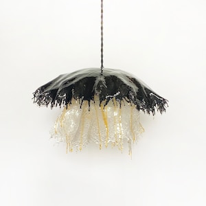 May include: A black and white pendant light with a unique, dripping design. The light fixture is made of a black material with a white, translucent, and textured material hanging from it.