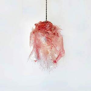 Op de afbeelding: Een roze en rode glazen hanglamp in de vorm van een bloem met een lang snoer dat aan het plafond hangt.