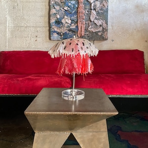 May include: A red and white lamp with a unique dripping design. The lamp is on a silver table with a geometric shape.