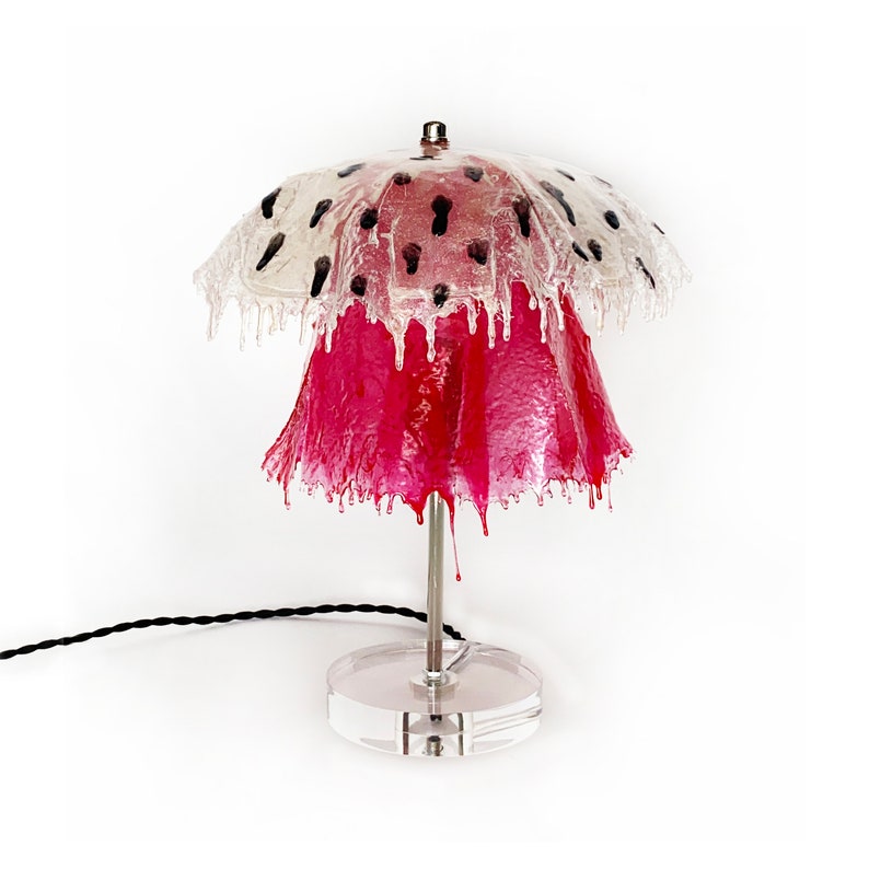 May include: A pink and clear table lamp with a unique dripping design. The lampshade is clear with black polka dots and the base is a clear cylinder.