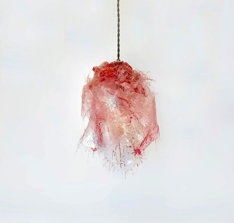 Op de afbeelding: Een roze en rode glazen hanglamp in de vorm van een bloem met een lang snoer dat aan het plafond hangt.