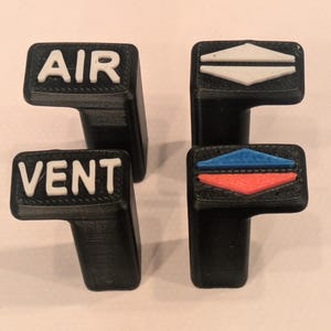 May include: Four black plastic car vent control knobs. Two knobs have the words "AIR" and "VENT" in white lettering. The other two knobs have white, blue, and red directional symbols.